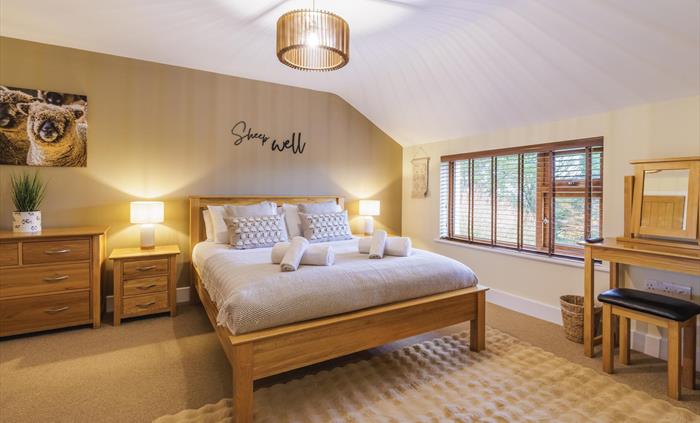 Sheep wall canvas above wooden chest of drawers, side tables with lamps either side of a king size bed with sheep cushions and a "Sheep Well" sign on